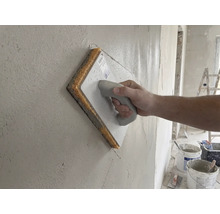 Hand verwendet ein Schwammbrett zum Glätten einer frisch verputzten Wand.