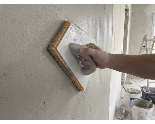 Hand verwendet ein Schwammbrett zum Glätten einer frisch verputzten Wand.