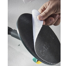 Eine Hand befestigt eine weiße Gitterschleifscheibe auf dem schwarzen runden Schleifteller eines Trockenbauschleifers.