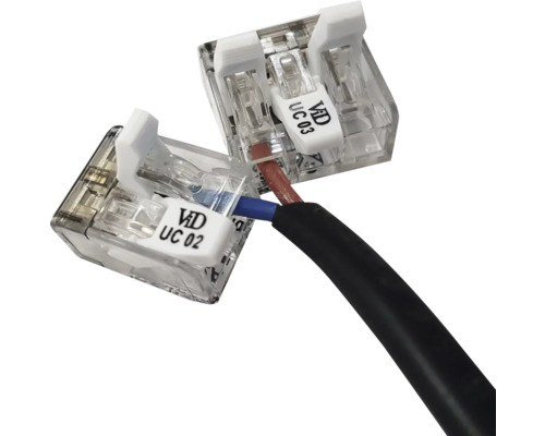 Transparente Verbindungsklemmen für elektrische Kabel mit weißen Hebeln, angeschlossen an ein schwarzes Kabel mit einer blauen und braunen Ader.