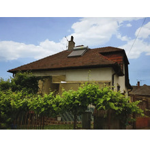 Wohnhaus mit einer Solarthermieanlage auf einem roten Ziegeldach, umgeben von grünen Pflanzen.