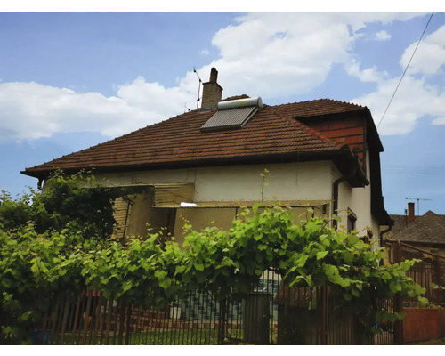Wohnhaus mit einer Solarthermieanlage auf einem roten Ziegeldach, umgeben von grünen Pflanzen.