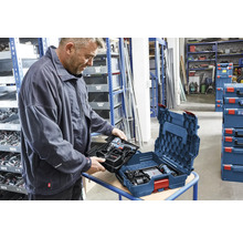 Ein Mann setzt eine Werkzeugeinlage mit Akku-Bohrschrauber in eine blaue Bosch L-BOXX in einem organisierten Lager mit Regalen ein.