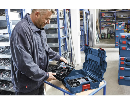 Ein Mann setzt eine Werkzeugeinlage mit Akku-Bohrschrauber in eine blaue Bosch L-BOXX in einem organisierten Lager mit Regalen ein.