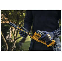 Person hält eine DeWalt 18 Volt Akku-Bandsäge mit Arbeitshandschuhen in einem Garten.