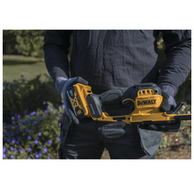 Person hält ein gelb-schwarzes DeWalt 18 Volt XR Akku-Gartengerät mit einem 5 Amperestunden Akku in einem Garten.