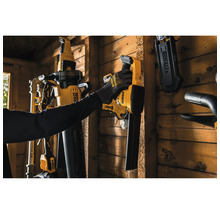 Eine Person hängt ein DeWalt Akku-Laubgebläse an eine Holzwand in einem Geräteschuppen neben anderen montierten DeWalt Elektrowerkzeugen.