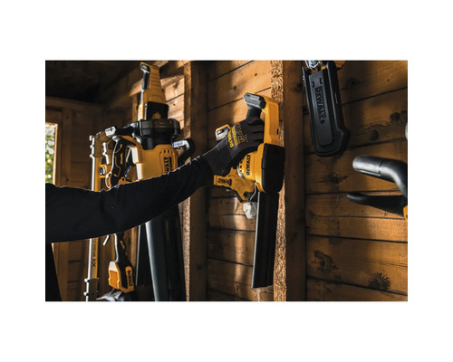 Eine Person hängt ein DeWalt Akku-Laubgebläse an eine Holzwand in einem Geräteschuppen neben anderen montierten DeWalt Elektrowerkzeugen.