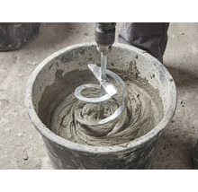 Ein Wendelrührer rührt grauen Mörtel in einem schwarzen Mörtelkübel an.