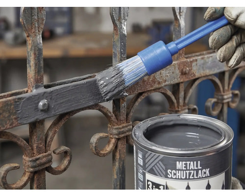 Metallschutzlack wird mit einem Rundpinsel auf einen rostigen Metallzaun aufgetragen.