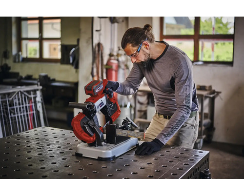 Eine Person benutzt eine Akku Metallbandsäge zum Schneiden eines Metallprofils auf einer Werkbank in einer Werkstatt.