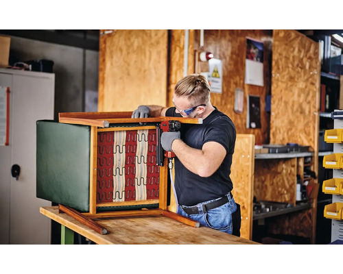 Handwerker befestigt Polsterung an einem Holzstuhl mit einem Drucklufttacker in einer Werkstatt.