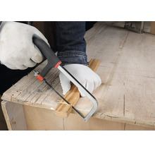 Person mit weißen Schutzhandschuhen schneidet eine Holzleiste mit einer kleinen Handsäge auf einer hölzernen Werkbank.