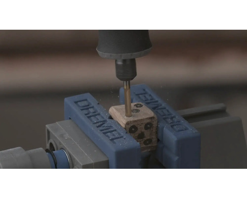 Dremel Rotationswerkzeug bohrt Löcher in einen Holzwürfel, der in einem Dremel Schraubstock eingespannt ist.