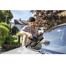 Ein Mann reinigt die Windschutzscheibe eines Autos mit einem Kärcher Fenstersauger im Freien.