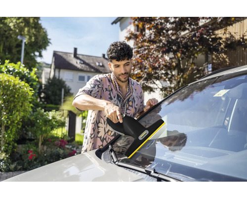 Ein Mann reinigt die Windschutzscheibe eines Autos mit einem Kärcher Fenstersauger im Freien.
