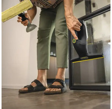 Person reinigt eine Glasscheibe mit einem Fenstersauger und einer Sprühflasche mit Wischer.