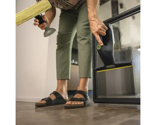 Person reinigt eine Glasscheibe mit einem Fenstersauger und einer Sprühflasche mit Wischer.