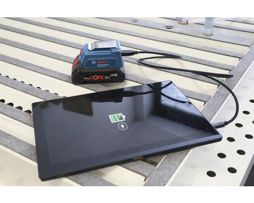 Bosch Professional USB Akku Adapter GAA 18 Volt 24 lädt ein Tablet mit einem ProCORE 18 Volt Akku auf einer Werkbank.