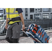 Handwerker mit Warnweste zieht eine Sackkarre beladen mit Bosch L-BOXX Werkzeugkoffern und einem Baustellenradio auf einer Baustelle.