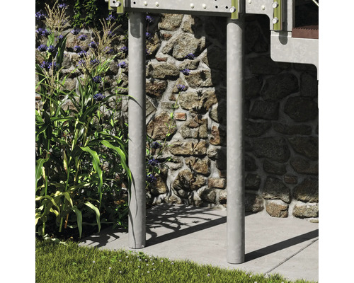 Zwei vertikale Metallstützen für eine Außentreppe oder ein Podest, vor einer Steinmauer neben Pflanzen und Gras platziert.