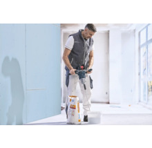 Handwerker rührt mit einem elektrischen Rührwerk Spachtelmasse in einem Kübel an, neben einem Sack Knauf Allround.