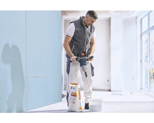 Handwerker rührt mit einem elektrischen Rührwerk Spachtelmasse in einem Kübel an, neben einem Sack Knauf Allround.