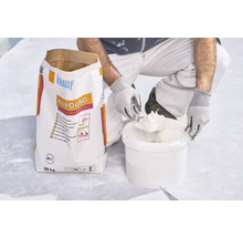 Handwerker entnimmt Spachtelmasse aus Kübel neben einem 20 Kilogramm Sack Knauf Allround 2 in 1 Universalspachtel.