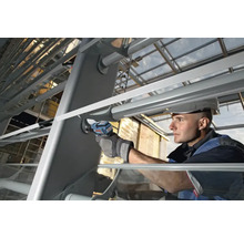 Handwerker mit Schutzhelm verwendet einen Akku-Schlagschrauber an einer Metallkonstruktion im Außenbereich.