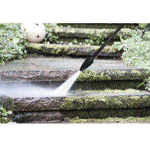 Ein Hochdruckreiniger reinigt vermooste Steinstufen im Garten mit einem kraftvollen Wasserstrahl.