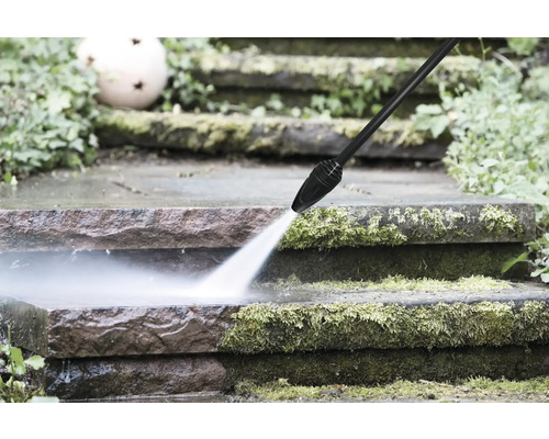 Ein Hochdruckreiniger reinigt vermooste Steinstufen im Garten mit einem kraftvollen Wasserstrahl.