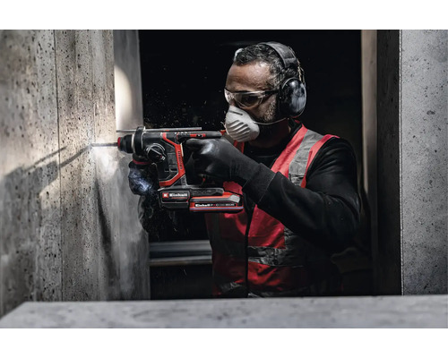 Handwerker bohrt mit einem Einhell Akku-Bohrhammer in eine Betonwand und trägt dabei Schutzausrüstung wie Gehörschutz und Atemschutzmaske.