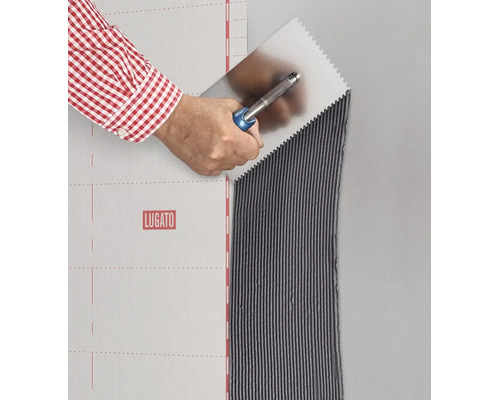 Eine Hand trägt mit einer Zahnspachtel Fliesenkleber auf eine Wand neben einer Lugato Abdichtungsbahn auf.