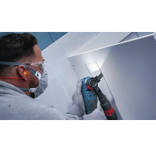 Handwerker mit Schutzbrille und Atemschutz beim Sägen einer Aussparung in eine weiße Platte mit einem Multifunktionswerkzeug