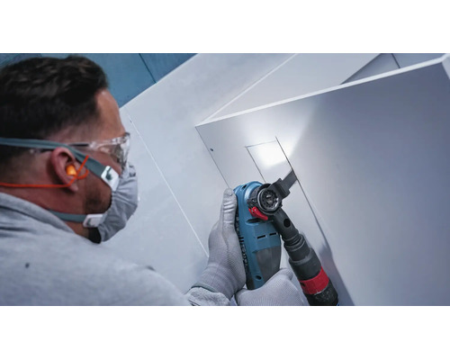 Handwerker mit Schutzbrille und Atemschutz beim Sägen einer Aussparung in eine weiße Platte mit einem Multifunktionswerkzeug