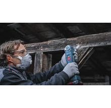 Handwerker mit Schutzausrüstung verwendet ein Akku Multitool zum Sägen an einem alten Holzbalken.
