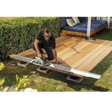 Ein Handwerker schneidet Holz-Terrassendielen mit einer Handkreissäge und Führungsschiene im Garten.