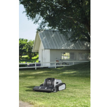 Lymow Mähroboter mit Raupenantrieb auf einem Rasen vor einem weißen Gartenhaus mit weißem Zaun.