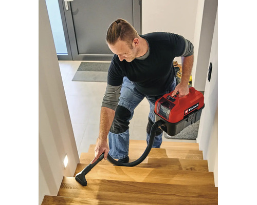 Ein Mann reinigt eine Holztreppe mit einem kompakten Akku-Nass-Trockensauger von Einhell.