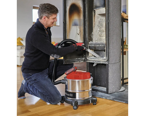 Ein Mann reinigt einen Kaminofen mit einem Einhell Akku-Aschesauger mit Metallbehälter auf Rollen.