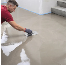 Ein Handwerker verteilt Ausgleichsmasse mit einer Glättkelle gleichmäßig auf einem Boden.