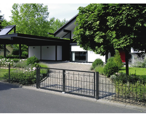 Schwarzer Metallzaun mit zweiflügeligem Tor vor einem modernen Garten und Haus mit gepflasterter Einfahrt.