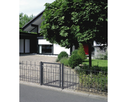 Schwarzer Metallzaun und Gartentor mit dekorativen Zierelementen vor einem modernen Haus mit gepflasterter Einfahrt und Garten.