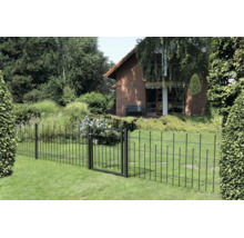 Schwarzer Metallzaun mit passendem Gartentor auf einem grünen Rasen vor einem Backsteinhaus und einem dichten Garten.