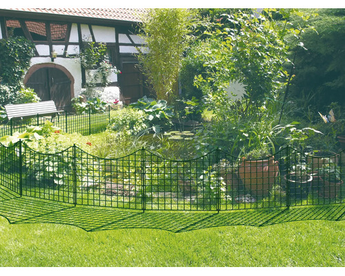 Grüner Metall-Steckzaun als Teichumrandung im Garten mit Pflanzen, Tontöpfen und einem Fachwerkhaus im Hintergrund.