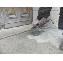 Eine Person reinigt eine Steinterrasse mit einer Far Tools Bürstenschleifmaschine Renovateur Exterieur vor einer Holztür.