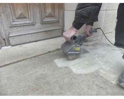 Eine Person reinigt eine Steinterrasse mit einer Far Tools Bürstenschleifmaschine Renovateur Exterieur vor einer Holztür.
