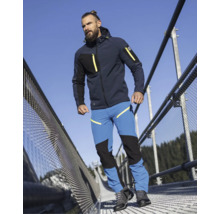 Mann in dunkelblauer Softshelljacke mit Kapuze und blauer Arbeitshose mit schwarzen Verstärkungen auf einer Metallbrücke.