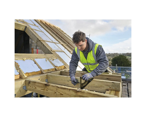 Handwerker markiert Holzbalken auf Dachbaustelle mit Sparrenwinkel und Bleistift. Er trägt Sicherheitsweste und Handschuhe.