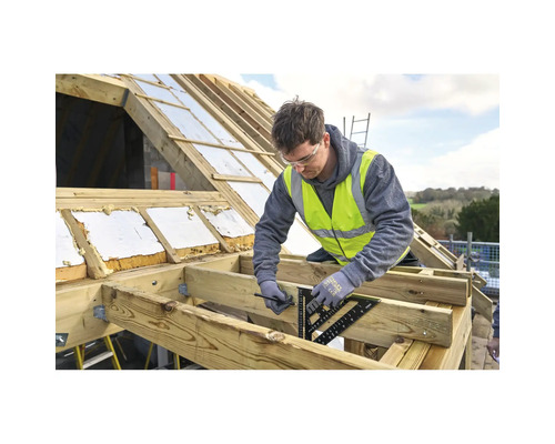 Handwerker markiert mit einem Sparrenwinkel und Bleistift einen Holzbalken auf einer hellen Dachbaustelle mit Holz- und Isoliermaterialien.
